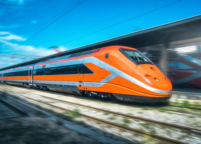 High-speed orange passenger train moving at railway station platform at sunset. Train station. Modern railway transportation concept with blurred motion effect. Railroad. Commercial transport